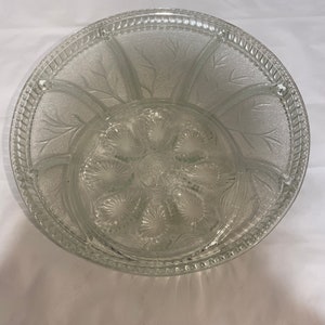May include: A clear glass serving bowl with a decorative etched design. The bowl has a central section with eight small indentations and a larger outer section with six sections.