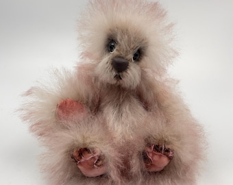 May include: A pink and white fluffy teddy bear with brown eyes and a brown nose. The bear is sitting with its paws tucked in front of it.