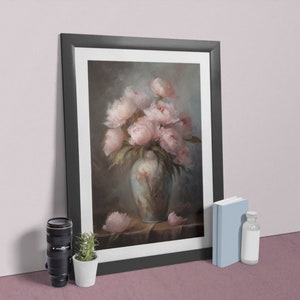 Op de afbeelding: Een ingelijst schilderij van een boeket roze pioenen in een blauw-witte vaas. Het schilderij heeft een donkere achtergrond en is geplaatst tegen een lichtroze muur.