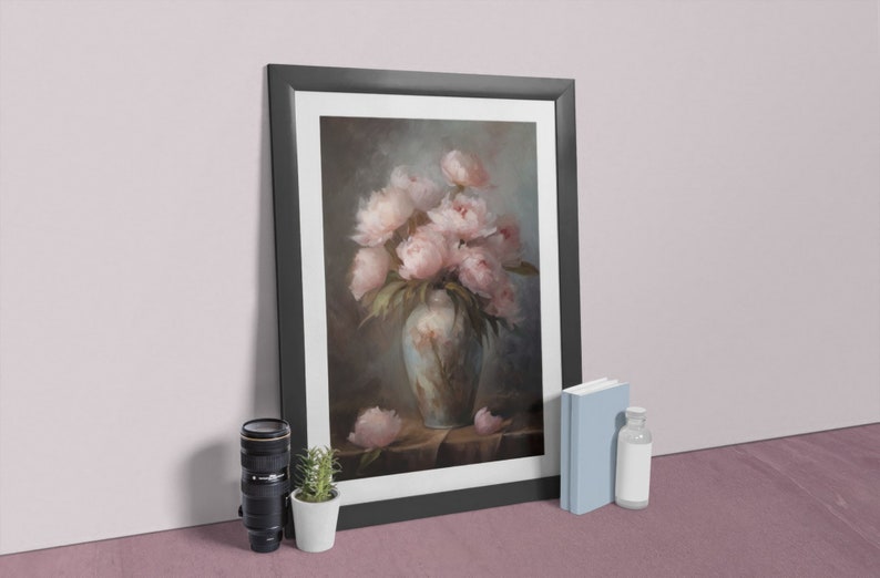 Op de afbeelding: Een ingelijst schilderij van een boeket roze pioenen in een blauw-witte vaas. Het schilderij heeft een donkere achtergrond en is geplaatst tegen een lichtroze muur.