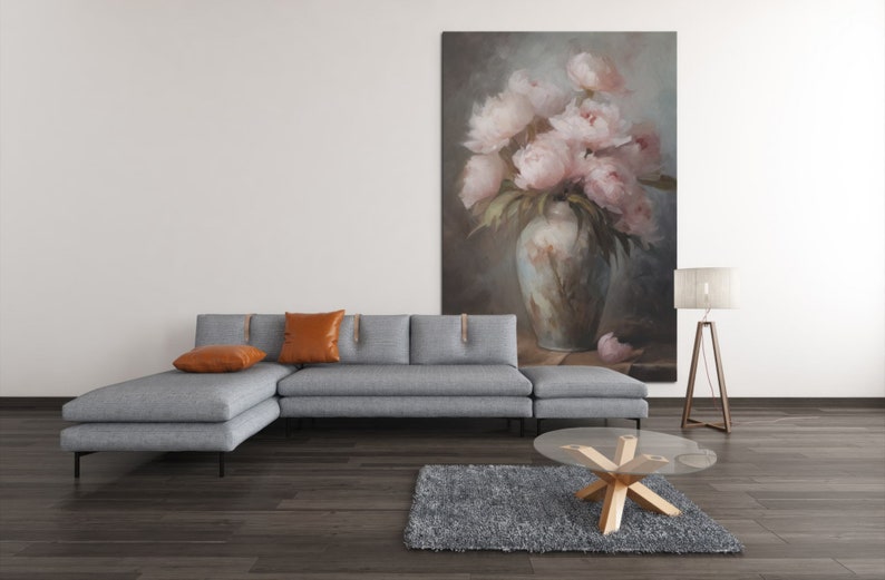 Op de afbeelding: Een grijze hoekbank met twee oranje kussens staat voor een schilderij van roze pioenen in een vaas. Een glazen salontafel met een houten onderstel staat op een grijs tapijt voor de bank.