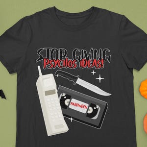 Könnte beinhalten: Schwarzes T-Shirt mit einem weißen Handy, einem Messer und einem VHS-Band. Der Text auf dem Shirt lautet "Stop Giving Psychos Ideas!" und "Halloween".