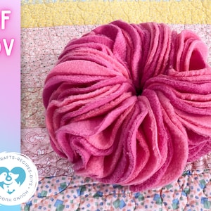 Könnte beinhalten: Ein rosafarbenes und rotes Fleece-Hundespielzeug in Donut-Form. Das Spielzeug besteht aus mehreren Schichten Fleece-Stoff, wodurch eine weiche und strukturierte Oberfläche entsteht.