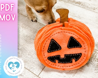 May include: A felt pumpkin dog toy in orange with a black felt face. The pumpkin has a stitched-on brown felt stem. A dog is sniffing the toy.