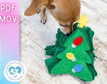 May include: A brown and white dog is sniffing a green felt Christmas tree toy with red, yellow, and blue lights. The toy is on a light brown wood floor. The text "PDF MOV" is in pink letters on a light blue and pink background. The text "DIGITAL DOWNLOAD" is in white letters on a light blue and pink background. A blue circle with white text says "DOG LOVIN' CRAFTS - RECIPES - DIYs - HOUND HUGGER".