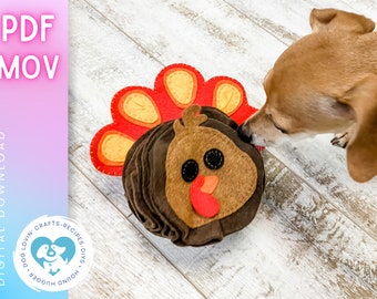 May include: A brown and tan dog sniffs a felt turkey toy with a red, orange, and yellow tail feathers. The toy is on a white wood floor.