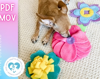 May include: A small brown dog is playing with a pink felt flower toy. The toy has a purple felt center and is surrounded by other felt flower toys in blue, yellow, and green.