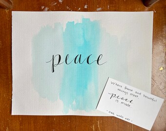 May include: A watercolor painting of the word "peace" in black calligraphy on a light blue background. A white card with the text "Where fierce and beautiful things meet, peace is made. ONE WORD ART" is placed on the bottom right corner of the painting.