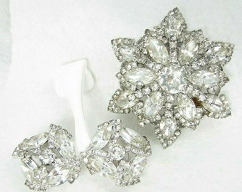 Può includere: Un set di gioielli vintage in strass con una grande spilla a forma di stella e un paio di orecchini abbinati. I gioielli sono realizzati con strass trasparenti incastonati in metallo argentato.