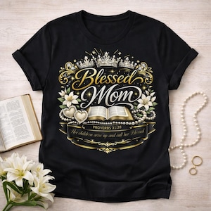 Op de afbeelding: Zwart T-shirt met een goud en wit ontwerp met de tekst "Blessed Mom". Het ontwerp bevat kronen, bloemen, harten en een open boek. De tekst "Proverbs 31:28" is ook opgenomen.