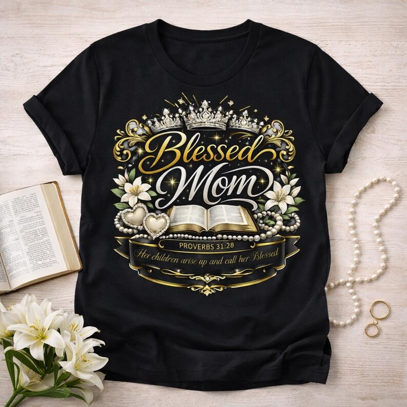 Op de afbeelding: Zwart T-shirt met een goud en wit ontwerp met de tekst "Blessed Mom". Het ontwerp bevat kronen, bloemen, harten en een open boek. De tekst "Proverbs 31:28" is ook opgenomen.