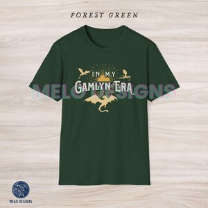 May include: Forest green t-shirt with a graphic design of three dragons flying around a sun with the text "In My Gamlyn Era".