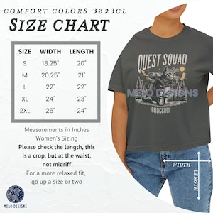 May include: Size chart for a gray cropped t-shirt with the text "Quest Squad" and a graphic of a cat wearing a backpack. The chart shows the width and length in inches for sizes S, M, L, XL, and 2XL.