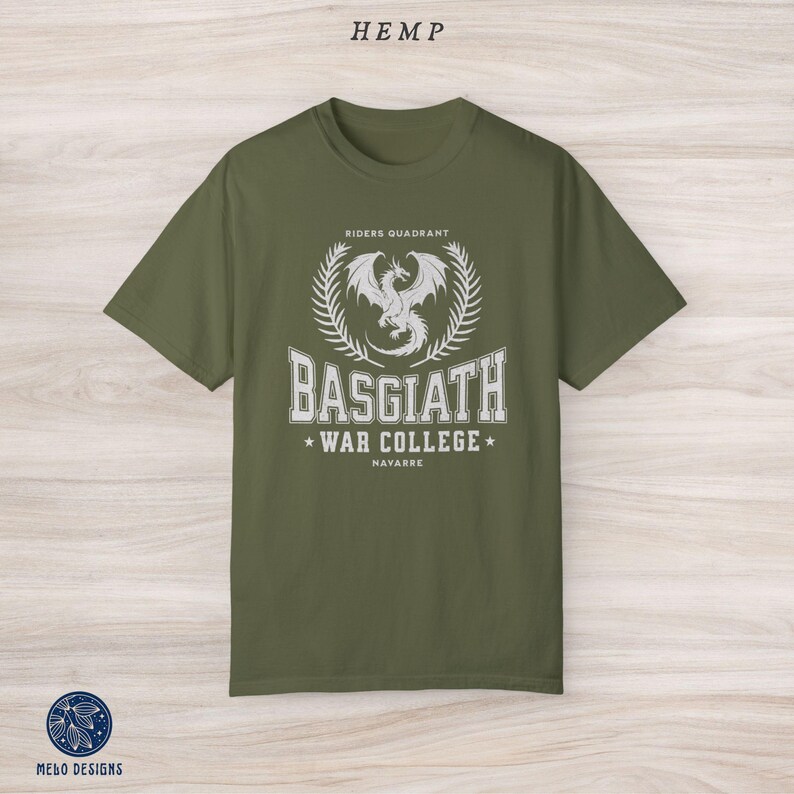 Puede incluir: Una camiseta verde con un dise&ntilde;o gr&aacute;fico blanco que presenta un drag&oacute;n, una corona de laurel y el texto "Riders Quadrant, Basgiath War College, Navarre".