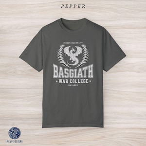 Puede incluir: Una camiseta gris oscuro con un dise&ntilde;o gr&aacute;fico blanco que presenta un drag&oacute;n, el texto "Riders Quadrant", "Basgiath War College" y "Navarre".