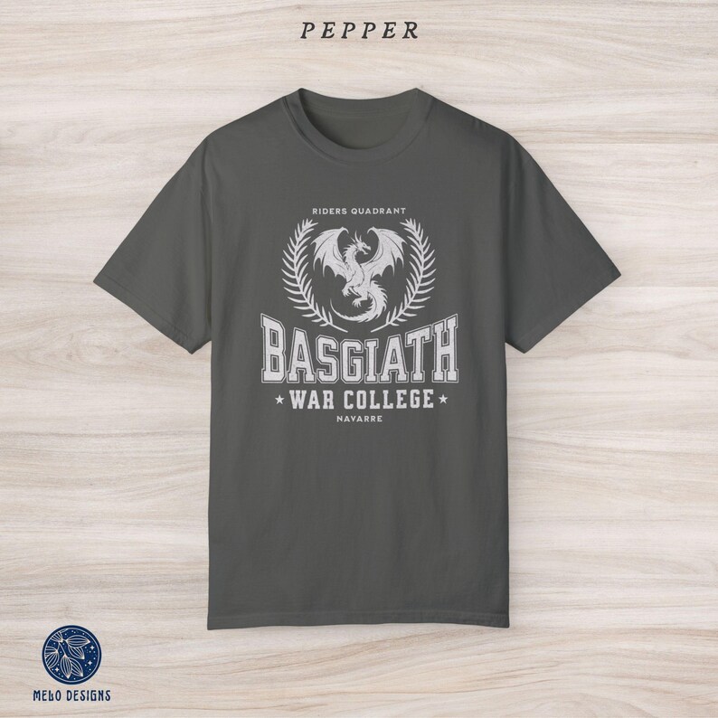 Puede incluir: Una camiseta gris oscuro con un dise&ntilde;o gr&aacute;fico blanco que presenta un drag&oacute;n, el texto "Riders Quadrant", "Basgiath War College" y "Navarre".