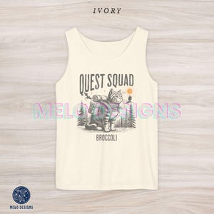 以下が含まれることがあります： バックパックを背負った猫のグラフィックと「QUEST SQUAD」と「BROCCOLI」のテキストが書かれた白いタンクトップです。