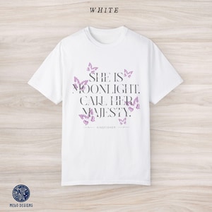 May include: White t-shirt with a graphic print of butterflies and the text "She is moonlight. Call her majesty." with the brand name "Kingfisher" printed below.