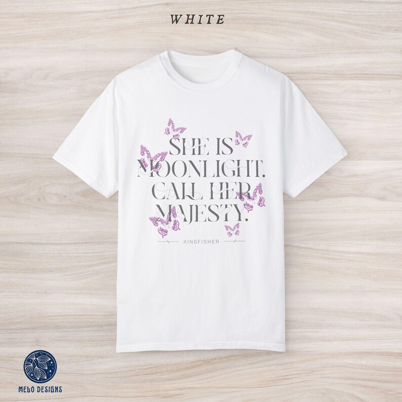 May include: White t-shirt with a graphic print of butterflies and the text "She is moonlight. Call her majesty." with the brand name "Kingfisher" printed below.
