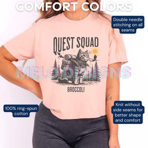 May include: A pink t-shirt with a black and white illustration of a cat wearing a backpack and the text "Quest Squad" and "Broccoli".