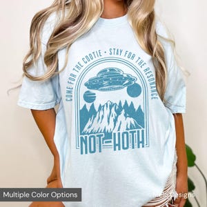 May include: A light blue t-shirt with a graphic design of a UFO flying over a mountain range. The text "COME FOR THE COOTIE STAY FOR THE RESONANCE NOT HOTH" is printed on the shirt.