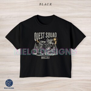 May include: Black cropped t-shirt with a graphic of a cat wearing a backpack and the text "Quest Squad" and "Broccoli".