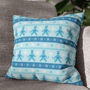 May include: A blue and white throw pillow with a repeating pattern of blue monsters with hearts on their chests. The pattern is reminiscent of a traditional Scandinavian Christmas sweater.