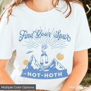 May include: White t-shirt with a blue graphic design. The design features the text "Find Your Spur" above a mountain scene with a seahorse-like creature and the words "on NOT-HOTH". Includes a small UFO and two gold-colored planets.