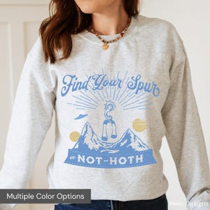 May include: A gray sweatshirt with a blue graphic design that says "Find Your Spur on Not-Hoth". The graphic features a stylized alien creature with a sunburst behind it.