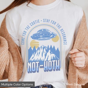 May include: White t-shirt with a blue and white graphic design featuring a UFO, mountains, and the text "COME FOR THE COOTIE STAY FOR THE RESONANCE NOT-HOTH".
