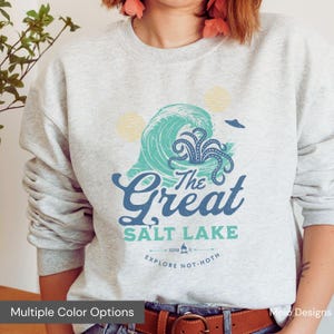 May include: A light gray sweatshirt with a graphic design featuring a turquoise wave with an octopus, the text "The Great Salt Lake", and the phrase "Explore Not-Hoth". The design includes two yellow suns and a small flying object.