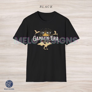 May include: Black t-shirt with a graphic design featuring a sun with rays, three dragons, and the text "In My Gamlyn Era".
