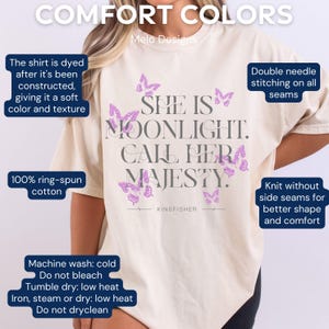 May include: A cream-coloured t-shirt with the text "She is Moonlight. Call Her Majesty." in grey with purple butterfly graphics. The shirt is made of 100% ring-spun cotton and has a comfortable fit.