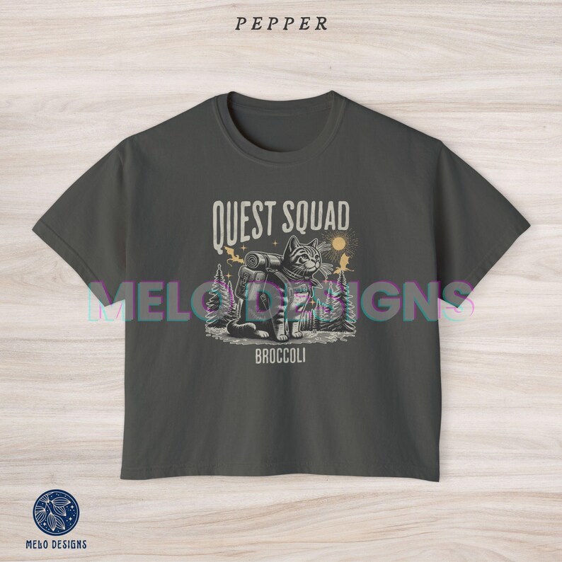 May include: A dark gray cropped t-shirt with a graphic of a cat wearing a backpack and the text "Quest Squad" and "Broccoli".