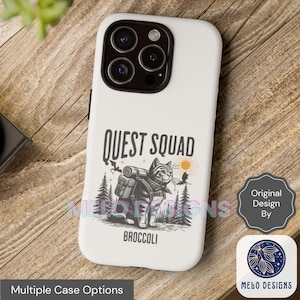 May include: White iPhone case with a black and white illustration of a cat wearing a backpack and the text "QUEST SQUAD BROCCOLI".