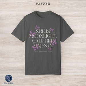 May include: A dark grey t-shirt with a purple butterfly design and the text "She is moonlight. Call her majesty." with the word "KINGFISHER" below the text.