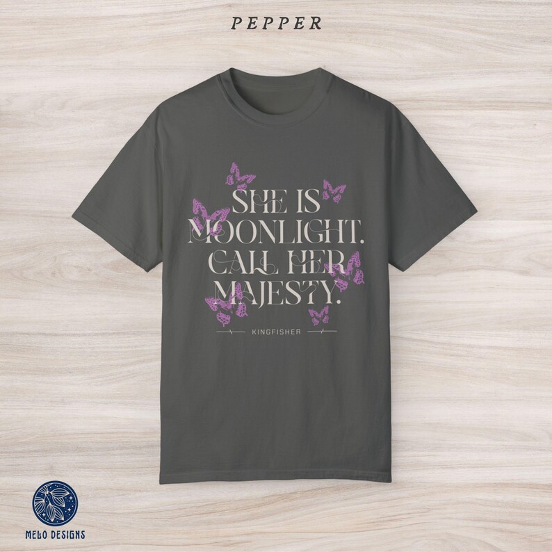 May include: A dark grey t-shirt with a purple butterfly design and the text "She is moonlight. Call her majesty." with the word "KINGFISHER" below the text.