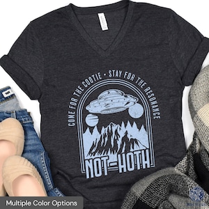 May include: A dark grey V-neck t-shirt with a blue graphic of a UFO flying over a mountain range. The text "Come for the cootie - Stay for the resonance Not Hoth" is printed on the shirt.