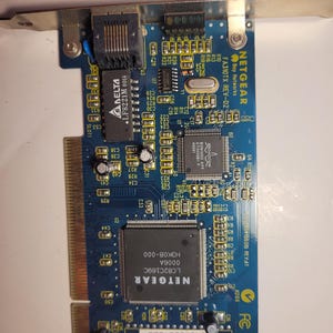 May include: A blue Netgear FA310TX REV-D2 network interface card featuring a metallic mounting bracket, an RJ45 Ethernet port, and various electronic components including a Broadcom chip, a Delta transformer, and a Netgear LC82C169C processor.