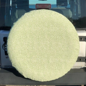 May include: A green and white patterned spare tire cover for a Jeep. The cover is made of fabric and has a white background with a green pattern.