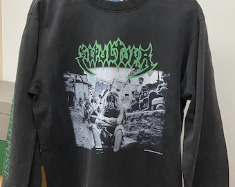 Puede incluir: Camiseta negra de manga larga con un gráfico que presenta el nombre de la banda "SKELETAL REMAINS" en verde y una imagen en blanco y negro de personas. La manga izquierda tiene el texto "SICKED POSSE" en verde.