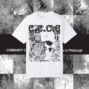 May include: White t-shirt with a black and white graphic design. The design features a face-like image composed of text and a large "C.C.C.C" at the top. The words "COMMUNITY C" and "e In Pittsburgh" are also visible.