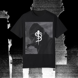 May include: Black t-shirt featuring a graphic print of a person wearing a gas mask and a symbol with a dagger.