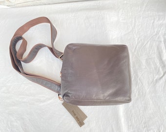 May include: A brown leather crossbody bag with a brown strap and a tag that says "The Bond".