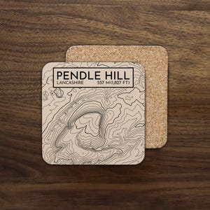 May include: Square coaster featuring a topographic map of Pendle Hill, Lancashire, with the text "PENDLE HILL" and "557 M (1,827 FT)". The coaster is beige with black contour lines and a cork backing.
