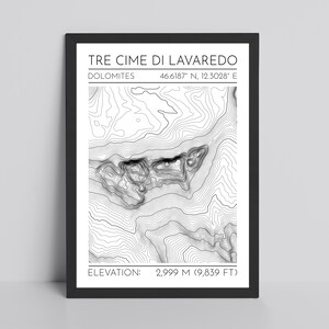May include: Black framed print featuring a topographic map of Tre Cime di Lavaredo in the Dolomites. The print includes the location's coordinates and elevation of 9,839 feet. The map is a detailed, grayscale illustration.