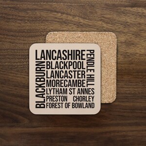 May include: Square coaster with the word "Lancashire" at the top, and the names of several towns and cities in the county of Lancashire, England, printed in black. The coaster is beige and sits on a cork coaster.