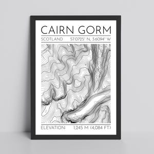 May include: Black framed print featuring a topographic map of Cairn Gorm, Scotland. The print includes the text "CAIRN GORM" and the coordinates 57.0725° N, 3.6094° W. Elevation is listed as 1,245 meters (4,084 feet).