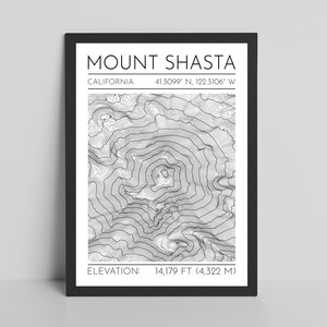 May include: A framed black and white print of Mount Shasta, California. The print includes the mountain's name, coordinates, and elevation of 14,179 feet (4,322 meters). The artwork features a detailed topographical map of the mountain.