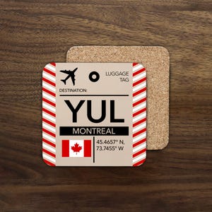 May include: A square cork coaster featuring a beige luggage tag design with red and white diagonal stripes on the sides. The text reads LUGGAGE TAG, DESTINATION: YUL, MONTREAL, and includes a Canadian flag icon and coordinates 45.4657° N, 73.7455° W.